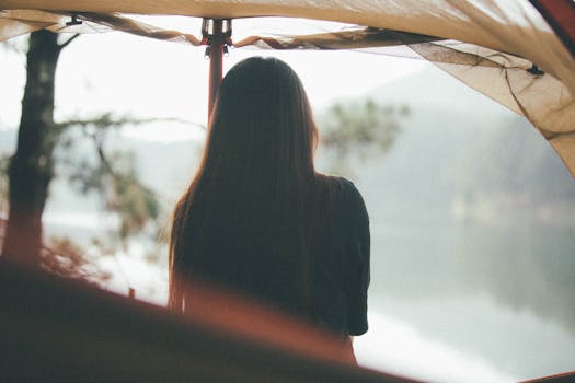 Femme de dos sous une tente, regardant un lac entouré de nature, évoquant un projet écolo et une routine capillaire naturelle