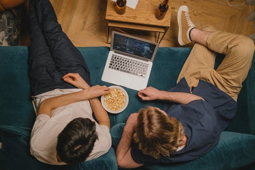Deux personnes assises sur un canapé, regardant un film sur un ordinateur portable avec un bol de pop-corn.