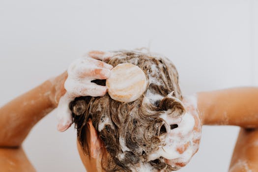 Femme lavant ses cheveux avec un shampoing solide, mousse et cheveux bouclés visibles.